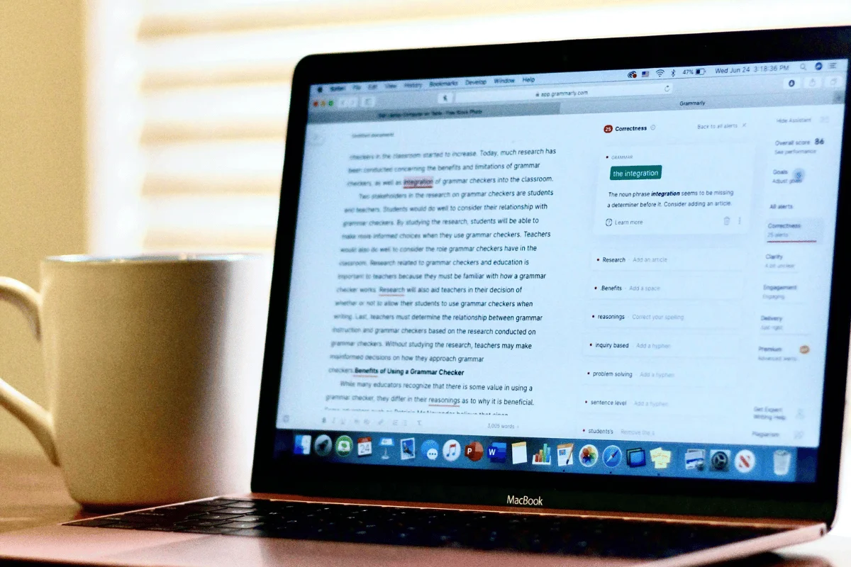 MacBook screen showing Grammarly editing suggestions next to a white coffee mug.