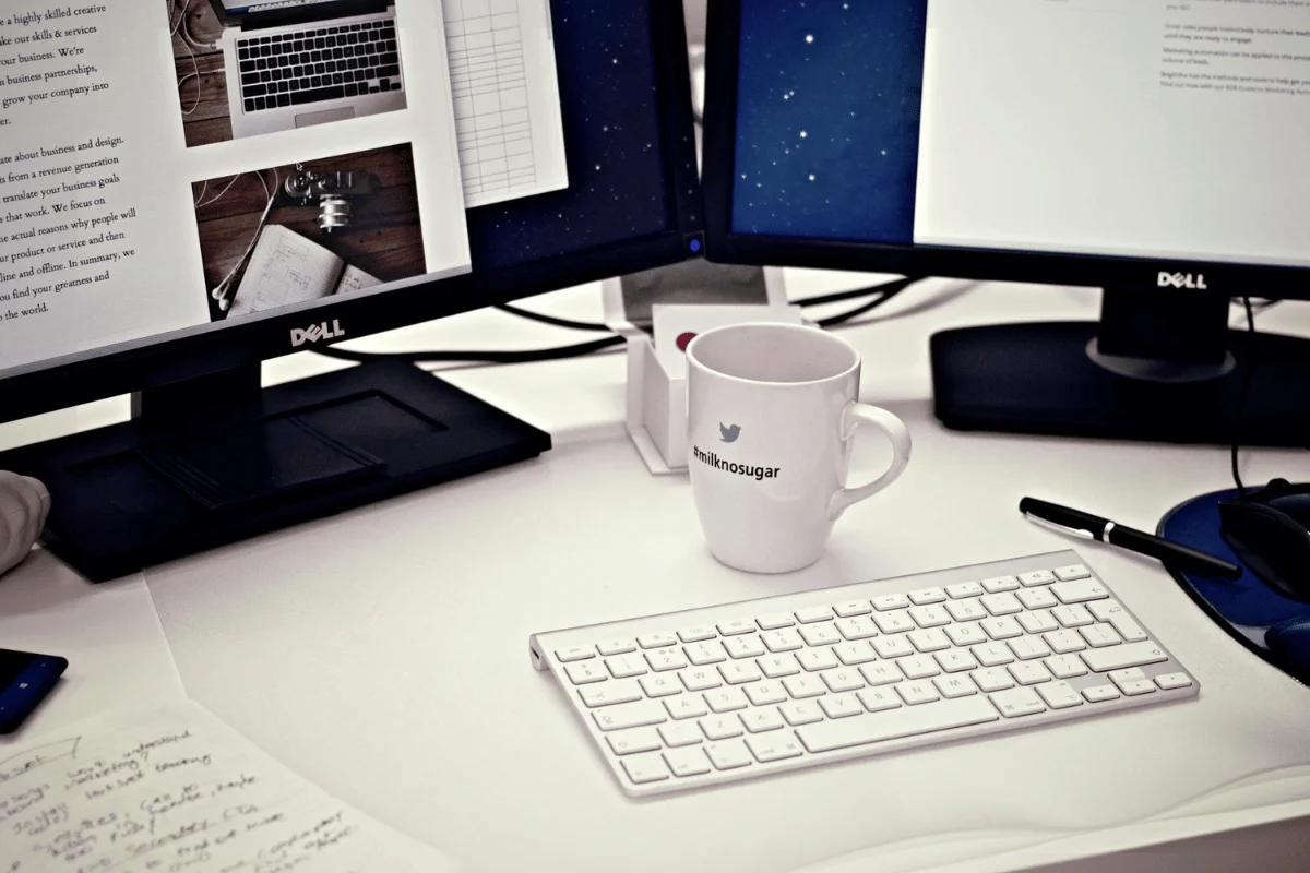 Dual Dell monitors with a white keyboard and a coffee mug on a desk.