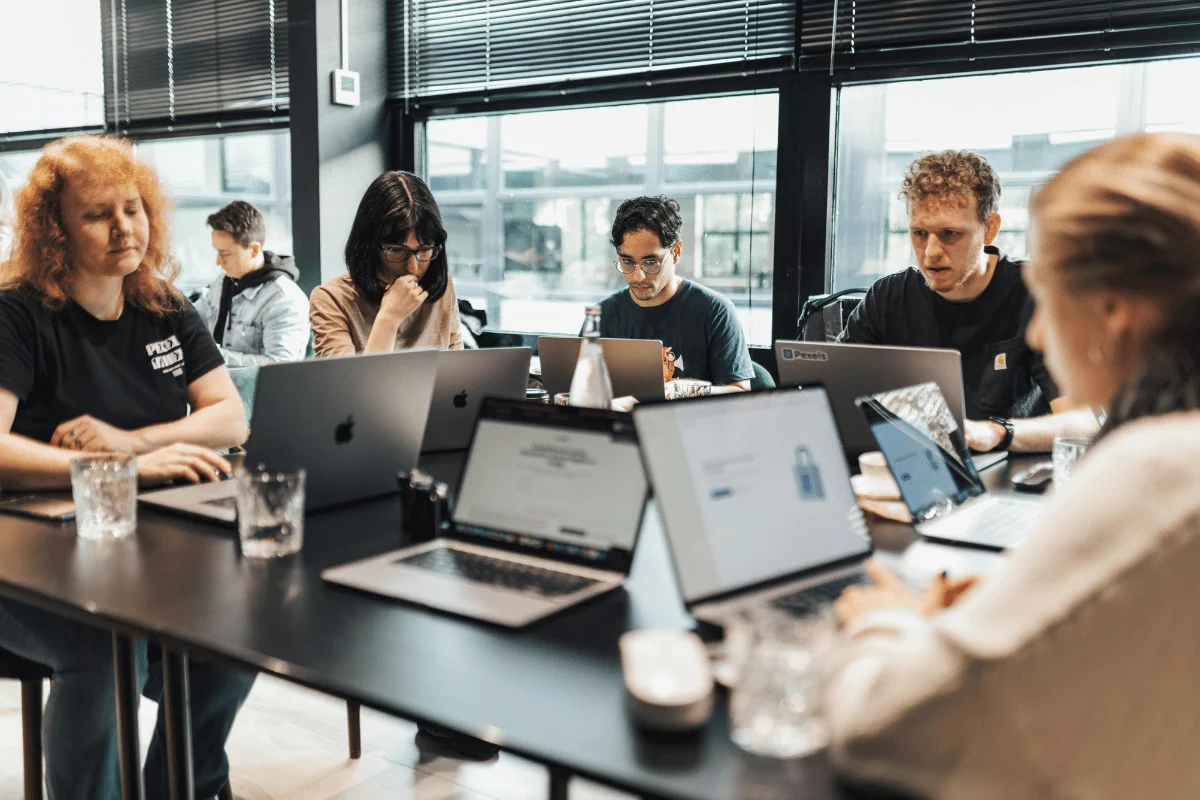 Group of people working on laptops during a team meeting in an office.