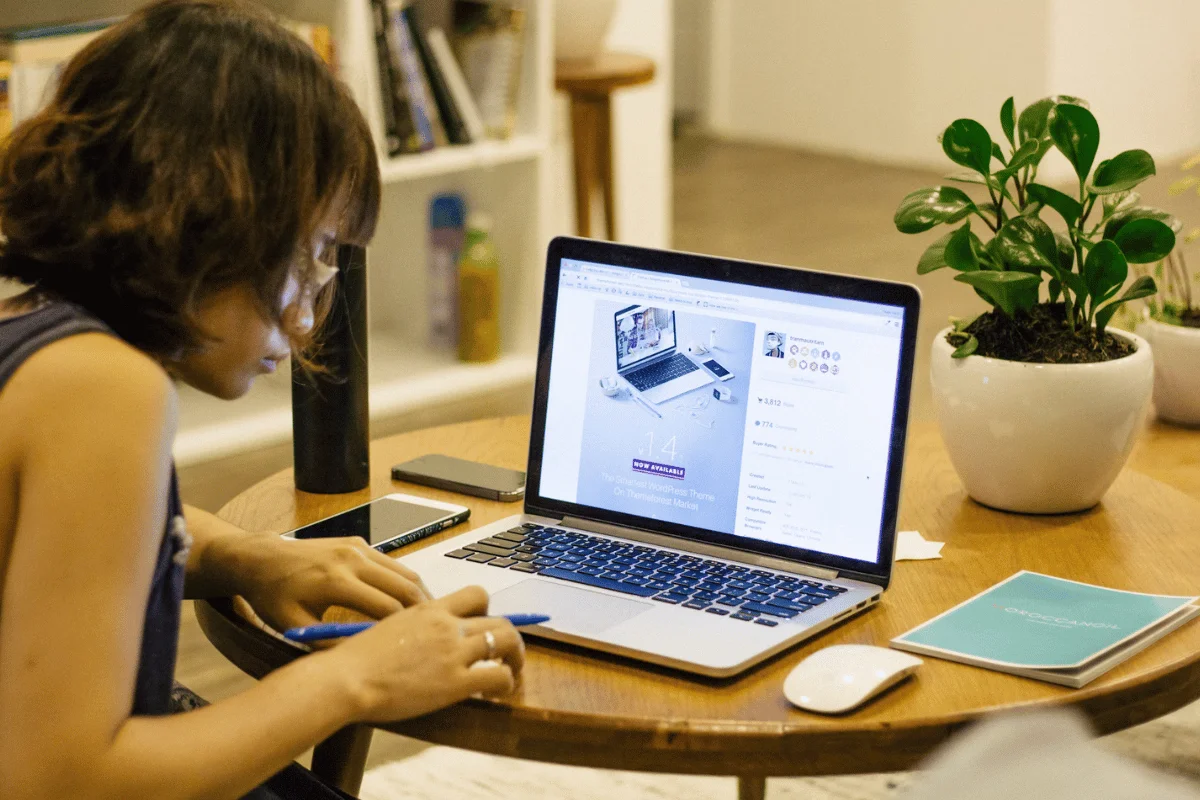 A woman sitting at a desk using a laptop, reviewing a WordPress theme called "The Simplest WordPress Theme" on her screen.