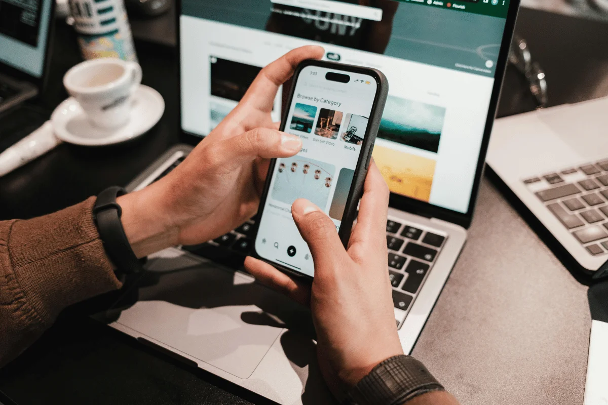 Person browsing categories on a smartphone while working on laptop.