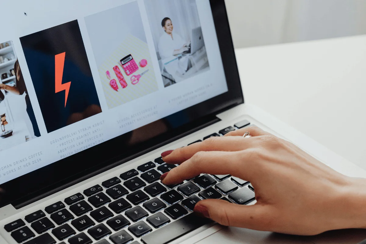 A person typing on a laptop with a visible hand and a screen displaying images of products and articles.