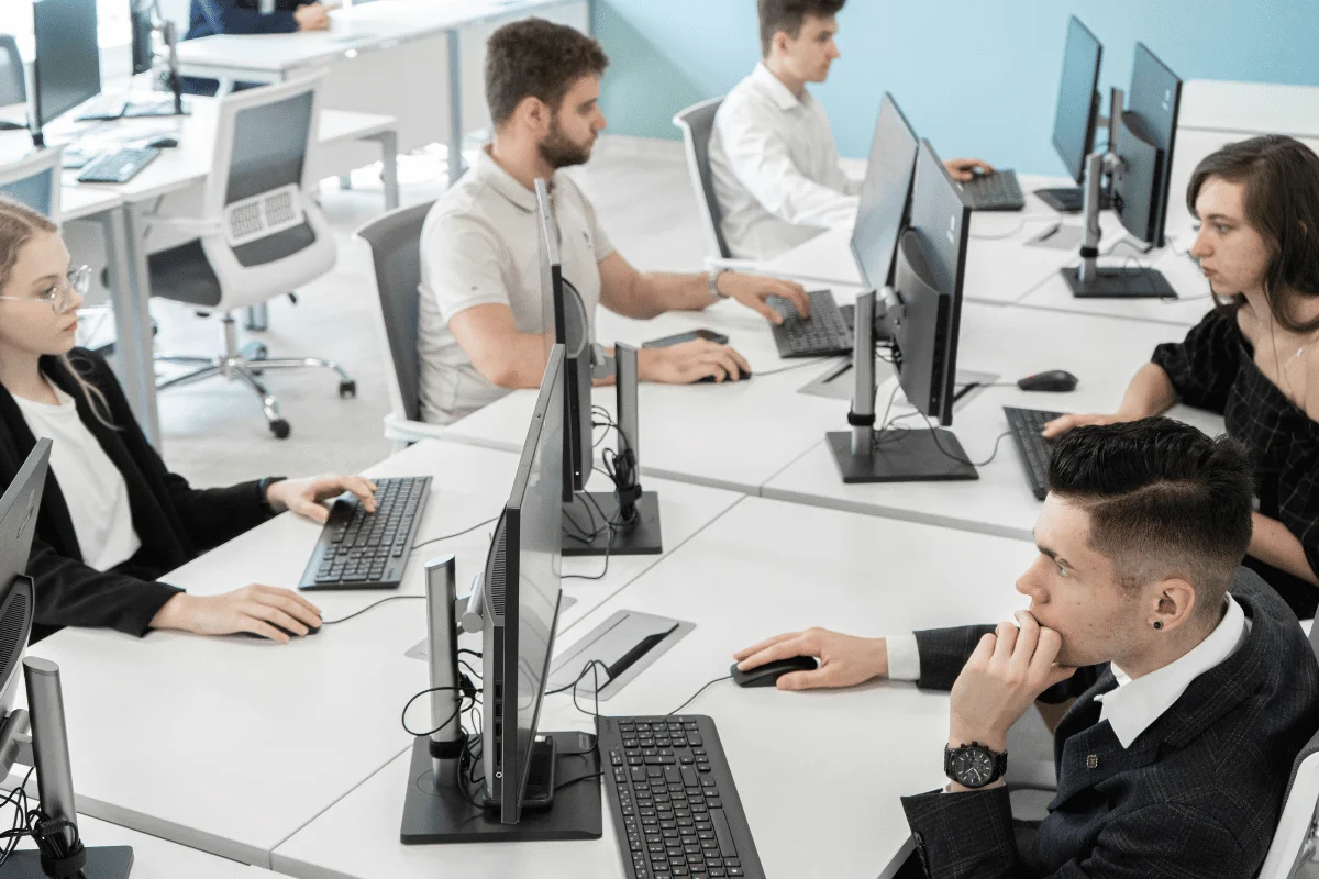 Office employees working at desktop computers in modern workspace.