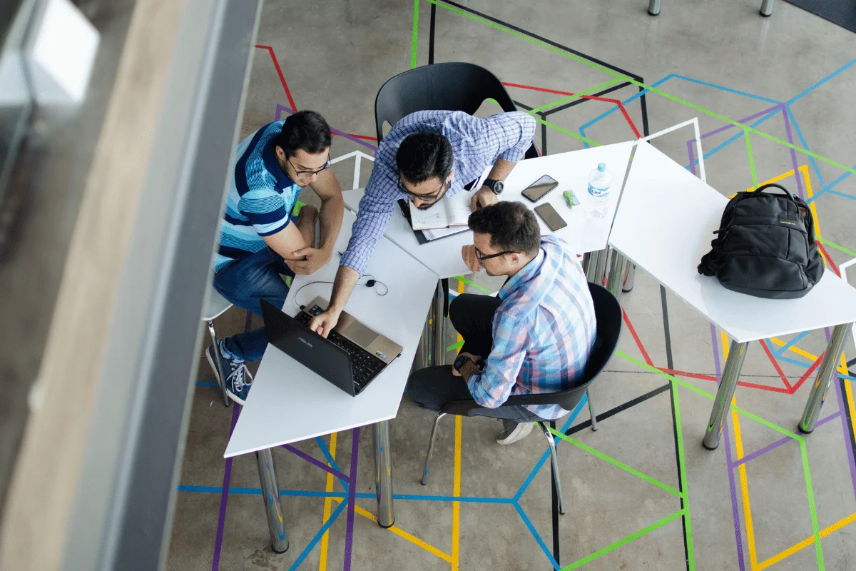 Three men collaborating on a laptop at a modern office.