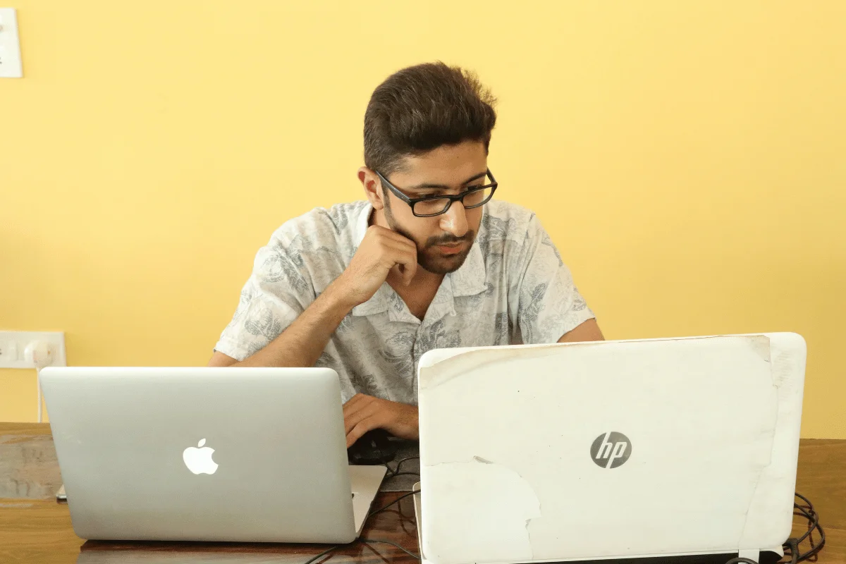 Man working on two laptops, Apple MacBook and HP device.