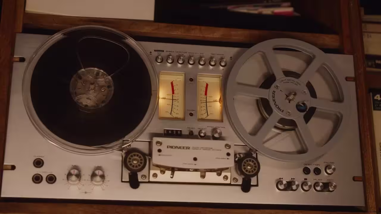 A vintage silver reel-to-reel tape recorder with dual reels, VU meters, and various control knobs, conveying a nostalgic and retro audio vibe.