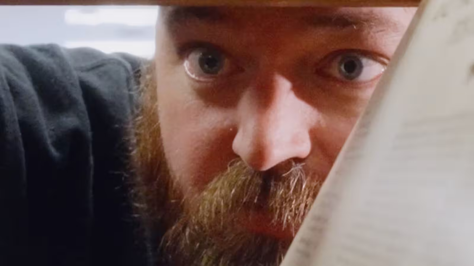 Close-up of a bearded man with wide eyes looking closely at a vinyl  or document.
