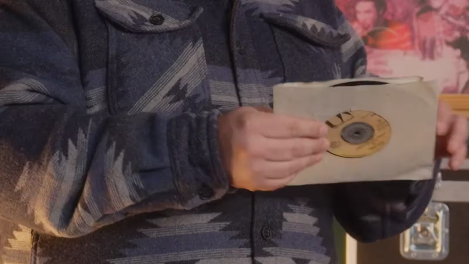 Person in patterned jacket holding a vinyl record partially inside a paper sleeve.