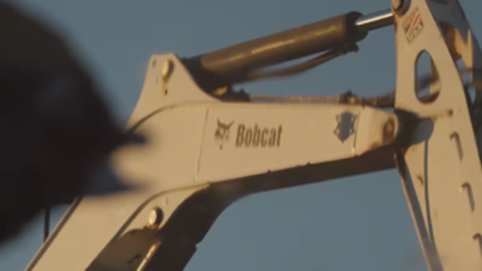 Close-up of a Bobcat brand construction machine arm against a clear sky.