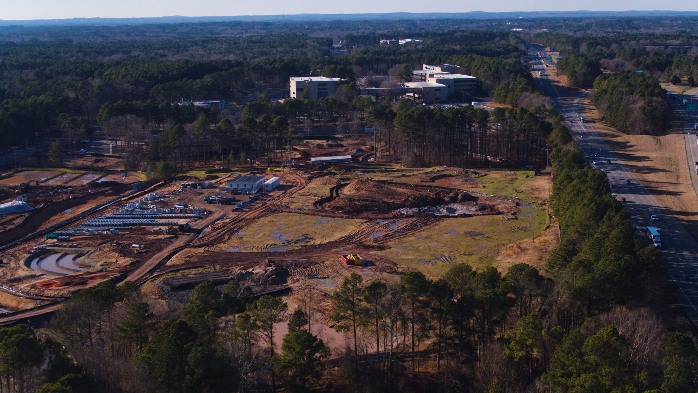 Aerial view of a construction site near a highway surrounded by trees and office buildings.