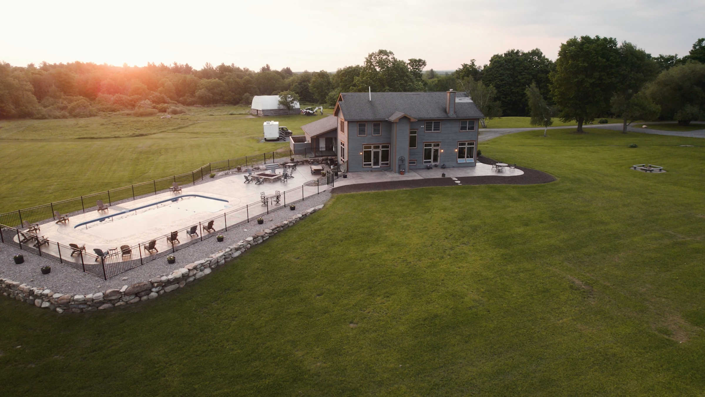 A large house with a fenced pool, patio seating, and expansive lawn at sunset.
