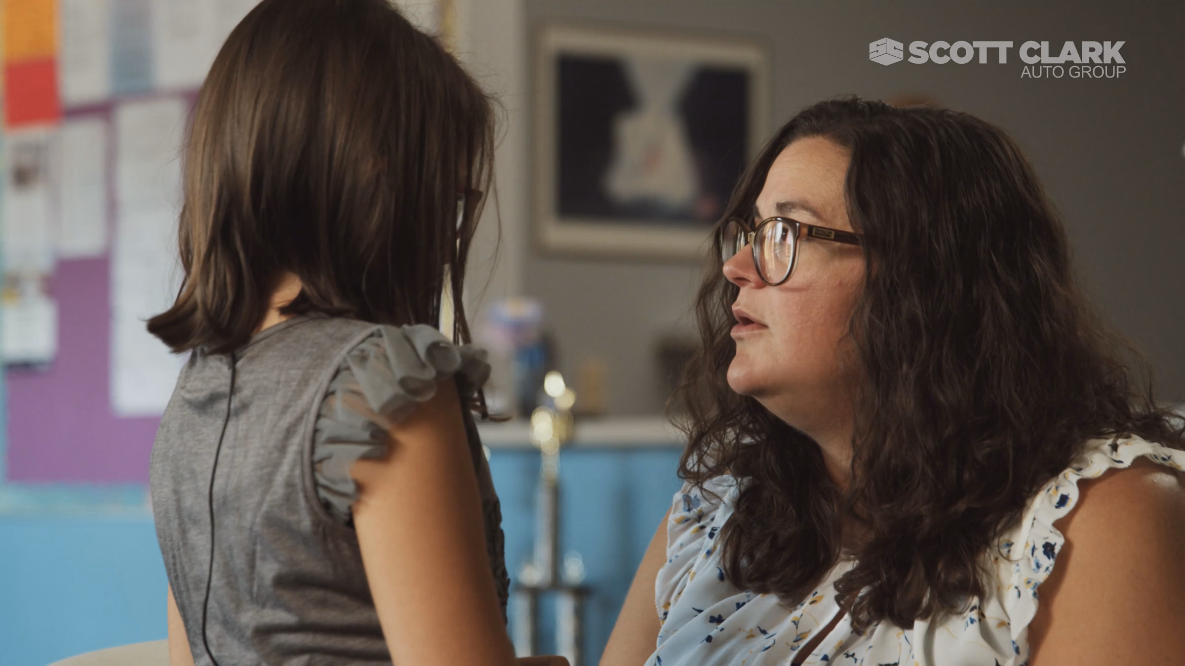 Woman wearing glasses talking seriously to a young girl in a casual indoor setting.