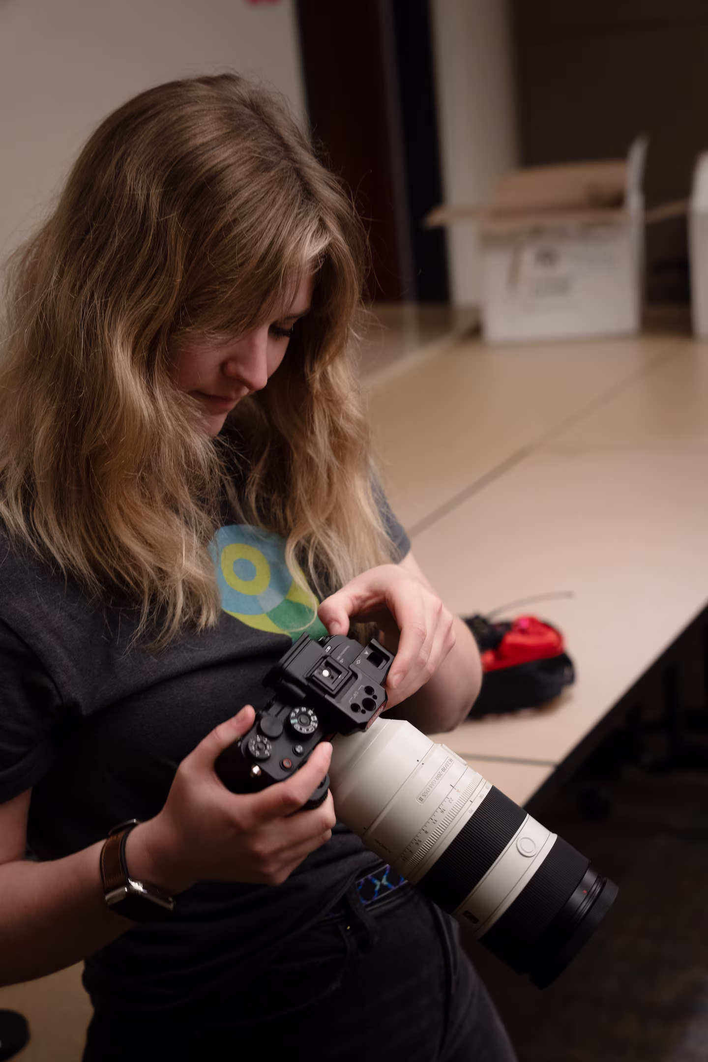 Woman with wavy hair holding and inspecting a professional camera with a large telephoto lens.
