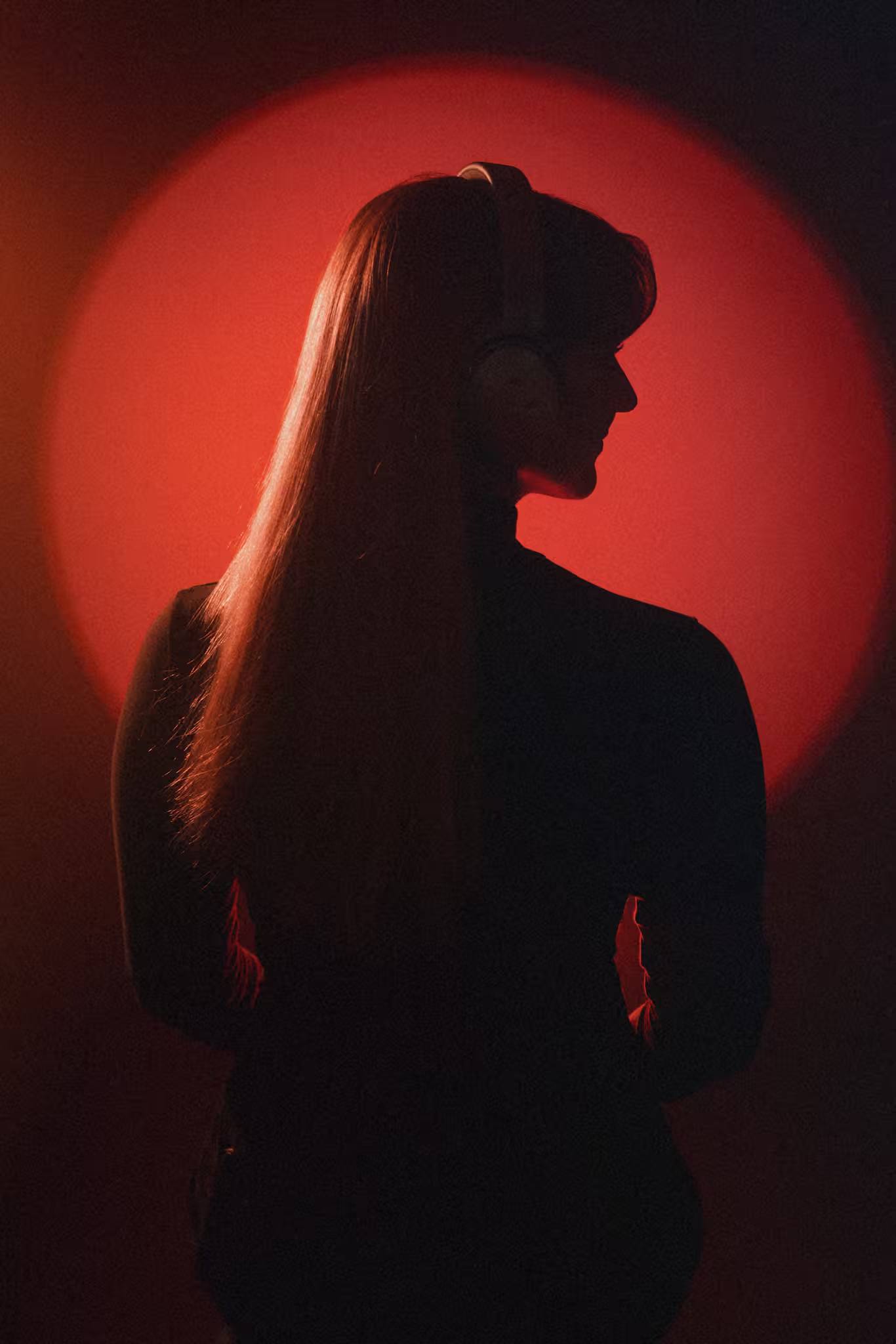 Silhouette of a person with long hair and headphones against a bright red circular background.