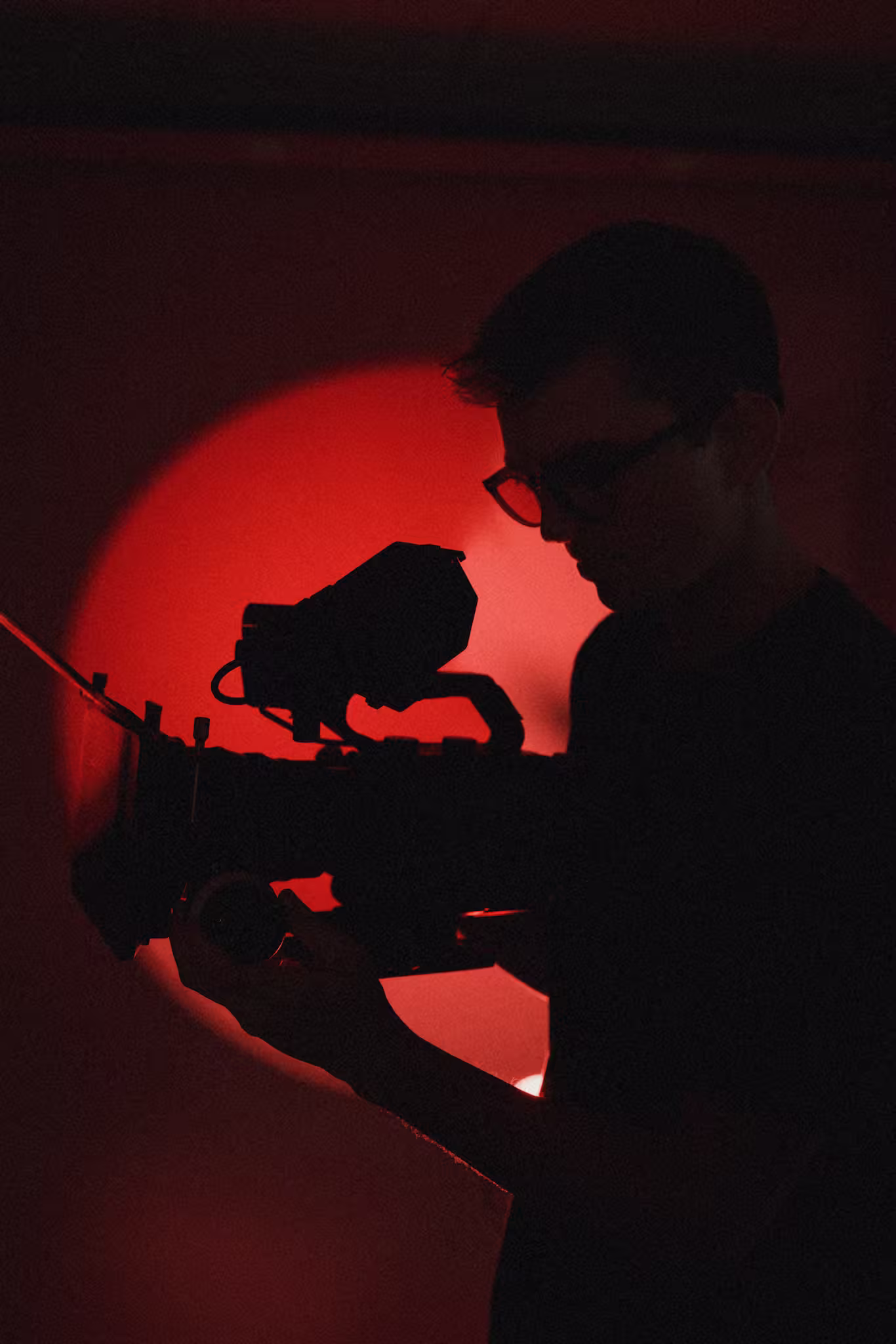 Silhouette of a person with glasses operating a professional video camera against a red light background.