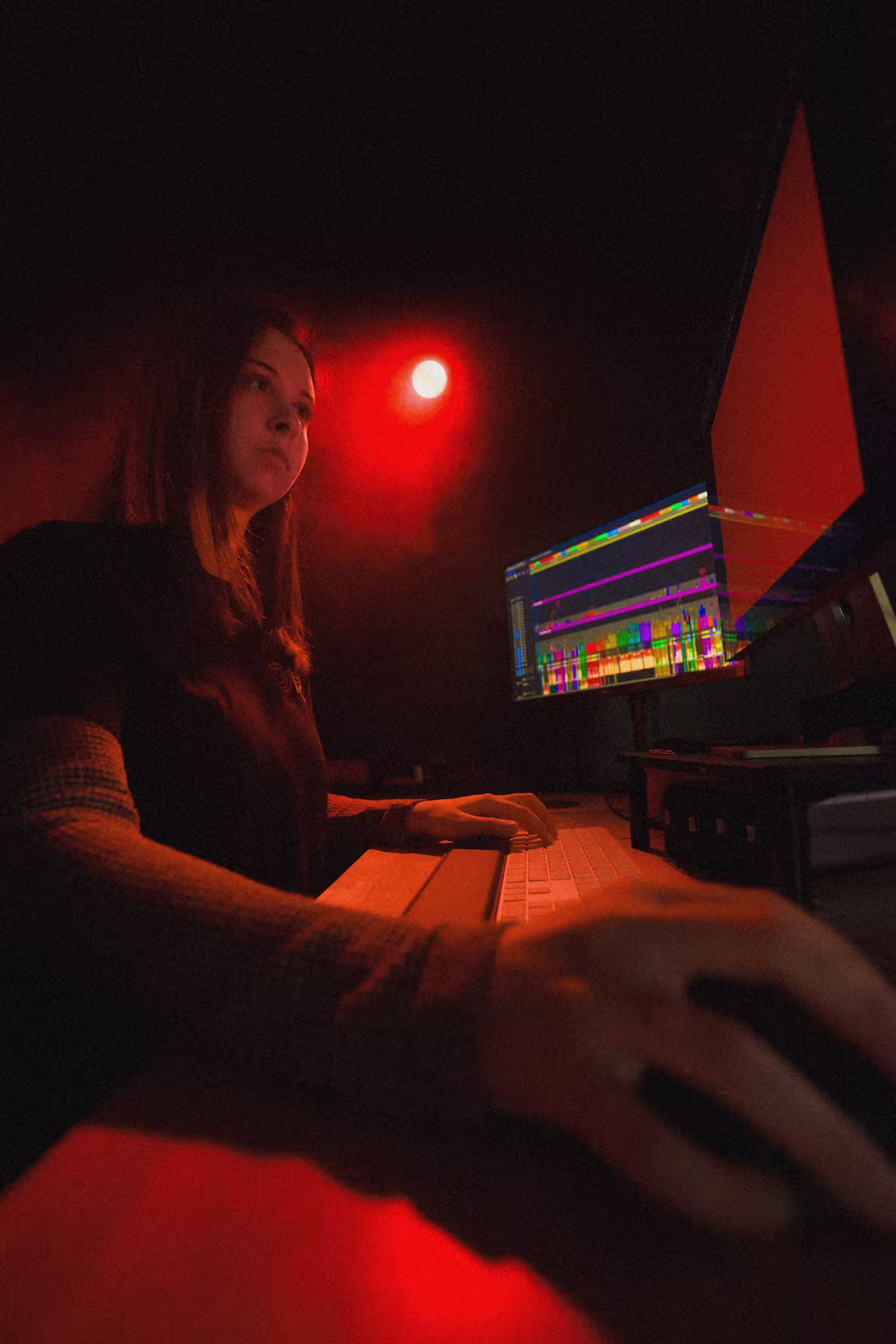 Person working on a computer with colorful data graphs on screen in a dim red-lit room.