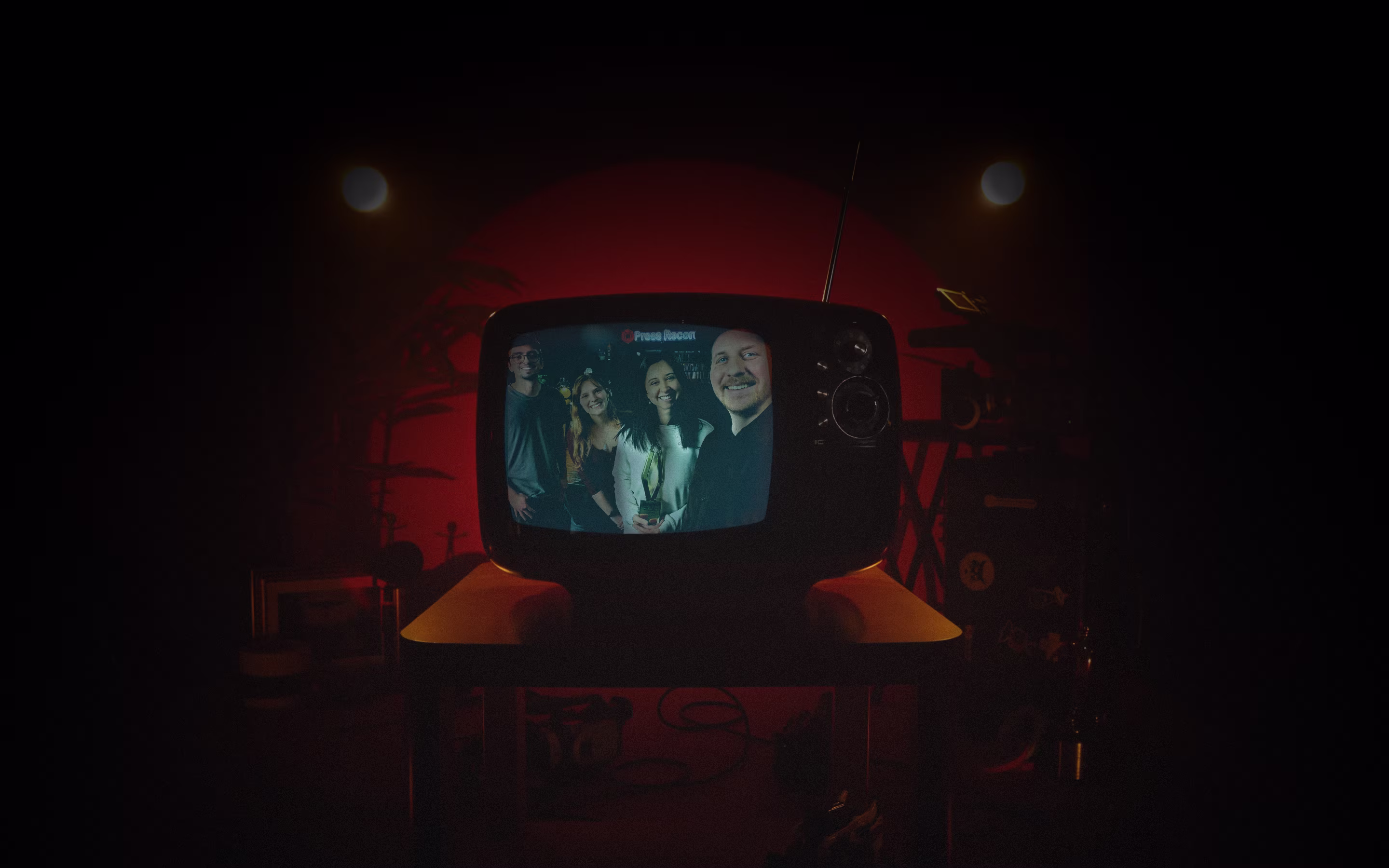 Retro TV on a table showing four smiling people posing for a photo in a dark room with red lighting.