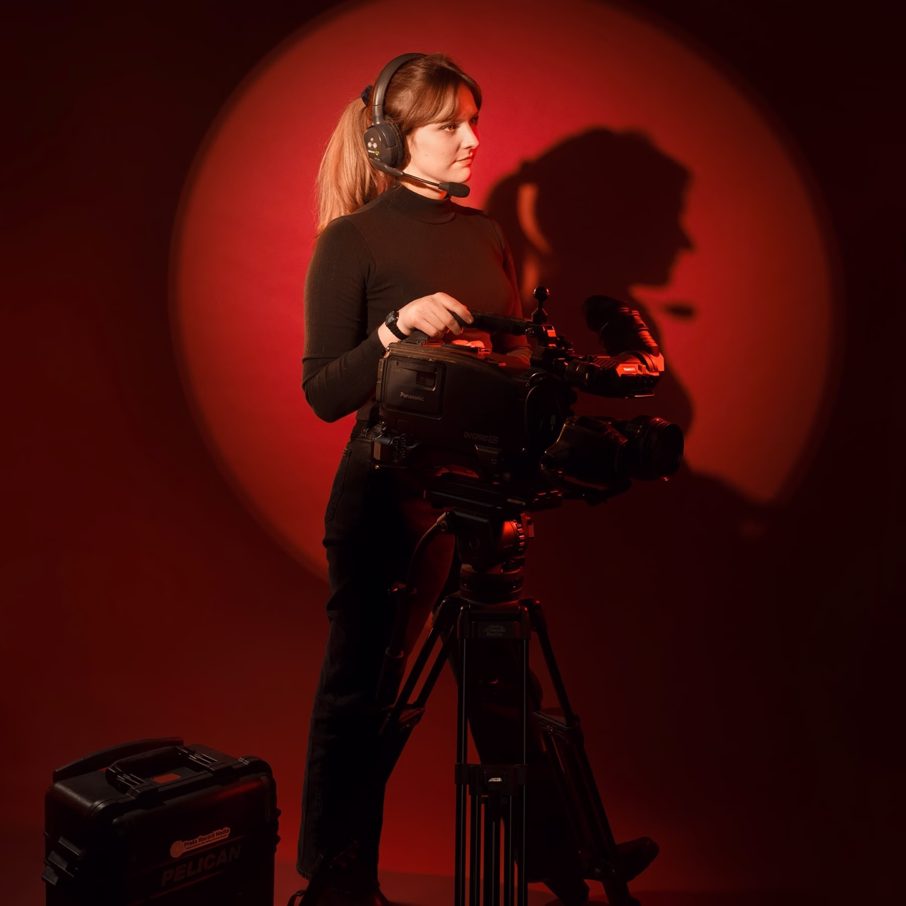 Woman in headset operating a professional video camera with red light and shadow backdrop.