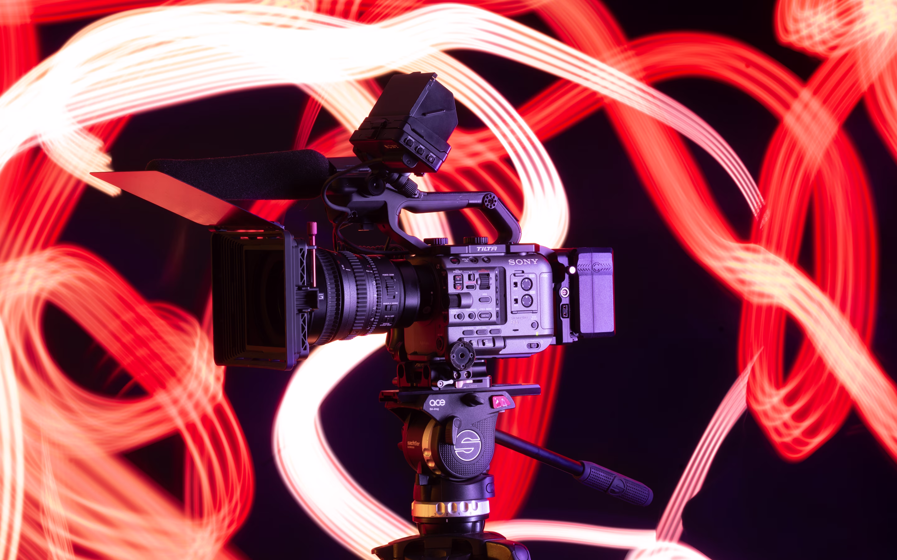 Professional Sony video camera on tripod with swirling red and white light trails in background.