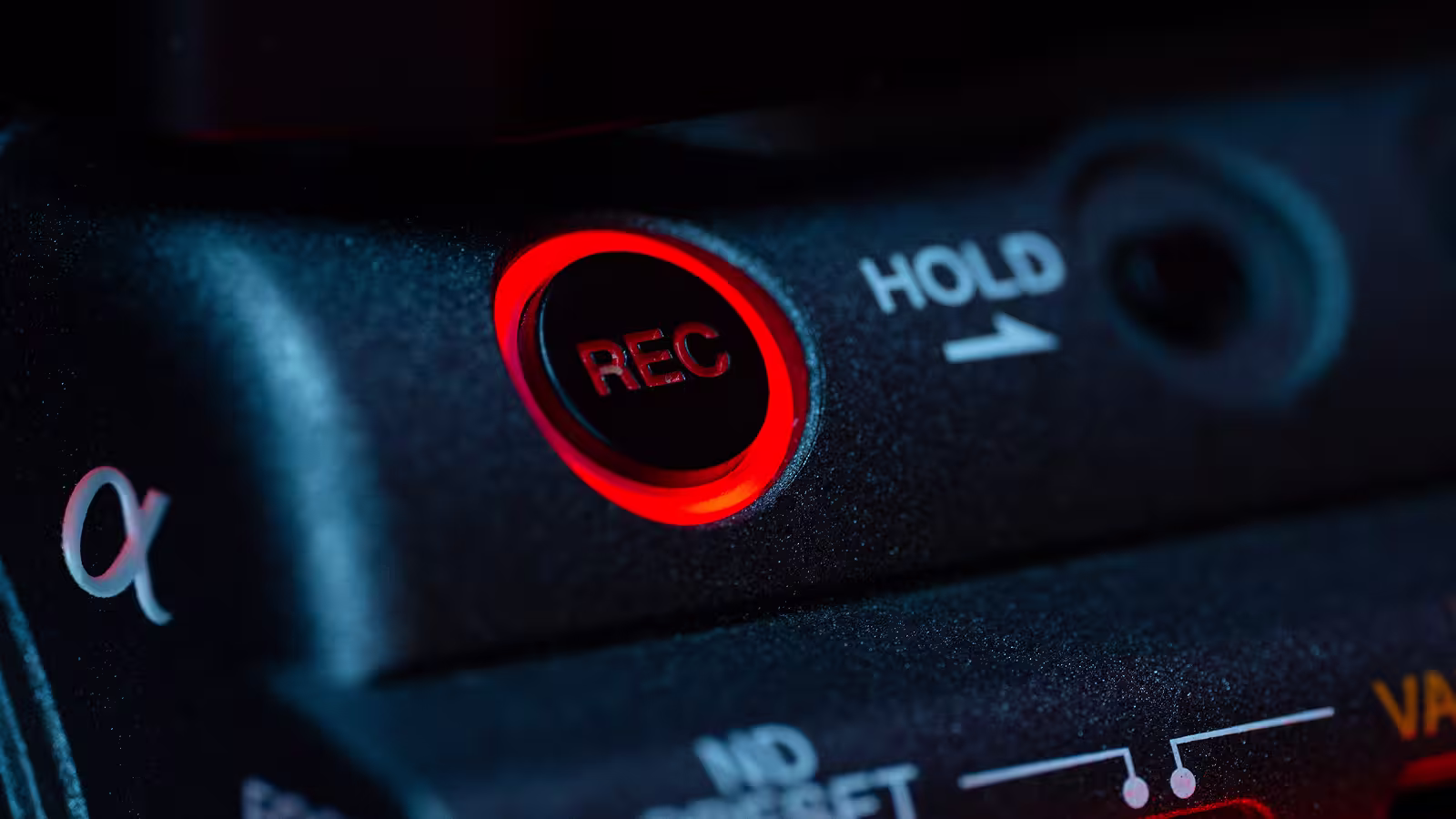 Close-up of a camera's red-lit REC button and HOLD switch on textured black surface.
