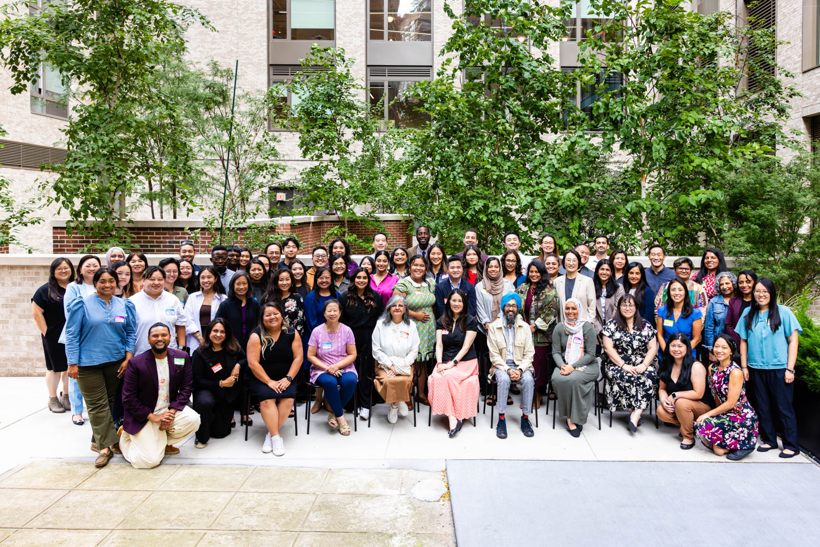 Large group photo of conference attendees outside among the trees. There are about 50 or more people gathered side by side.