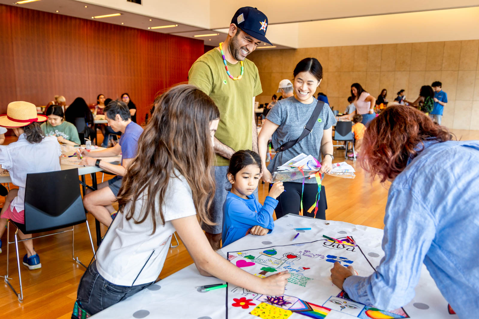 Two adults and two children smiling and focusing on crafting a colorful kite together with crafting supplies.