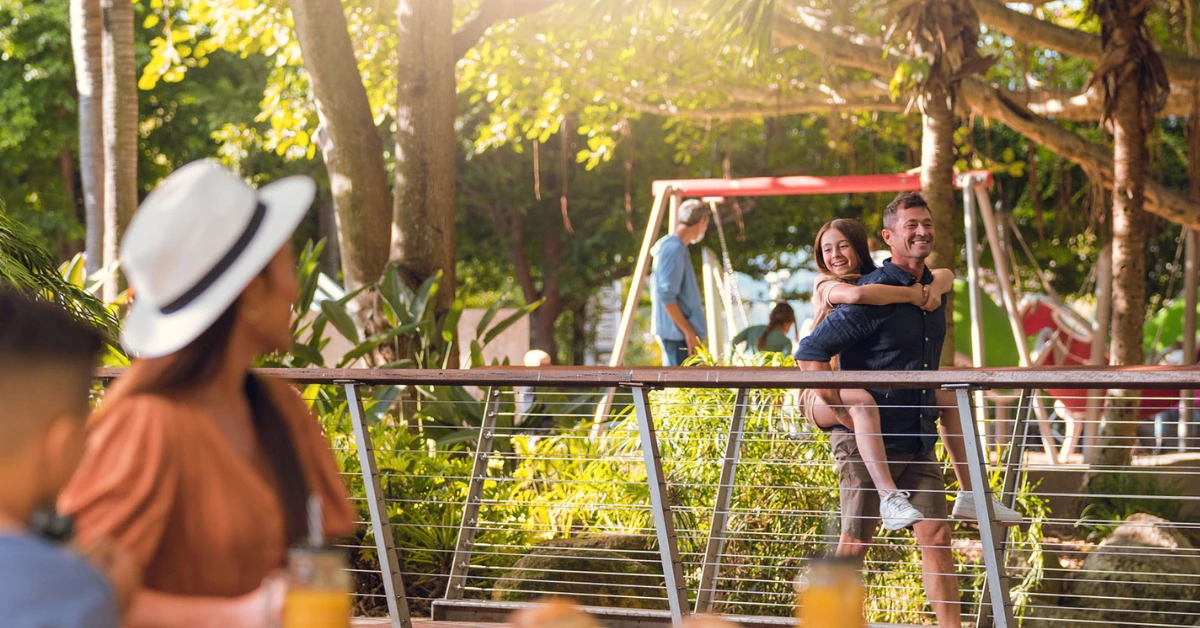 A father happily carries his daughter through South Bank playground as the mother looks on