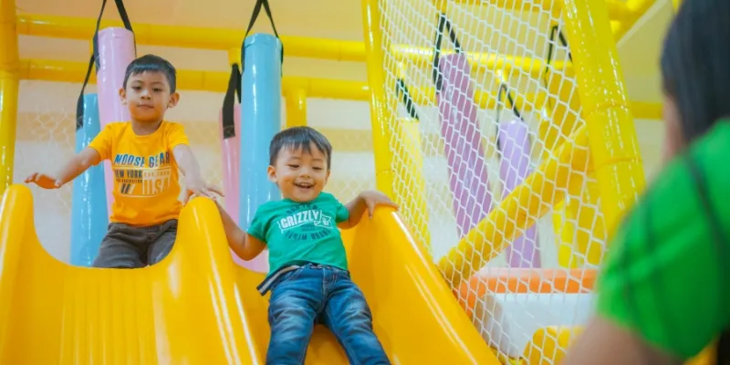 Kids on a slide enjoying an indoor play space.