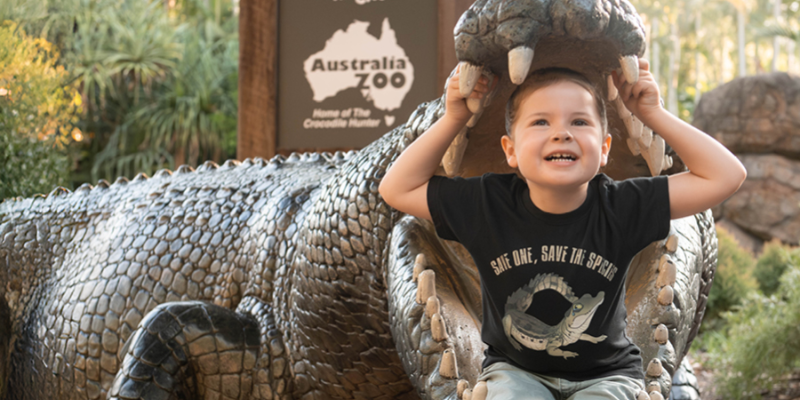 Child smiling, inside a crocodile statue at Australia Zoo, with zoo sign visible.