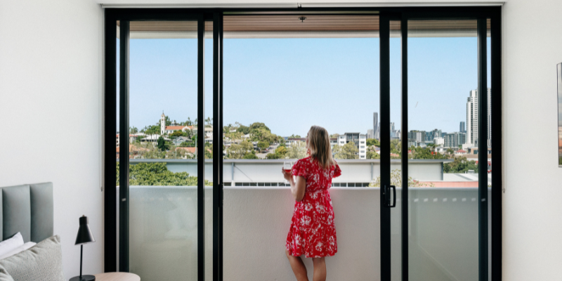Woman in red dress on balcony overlooking Brisbane city skyline with a glass of wine.