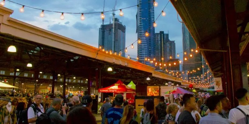 Visitors exploring Melbourne’s Winter Night Market with city lights and food stalls at Queen Victoria Market