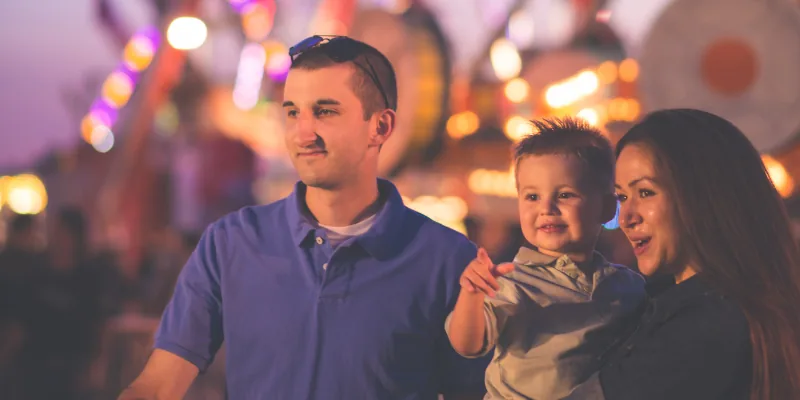 Family at a carnival with bright lights, featuring a father, mother and child.