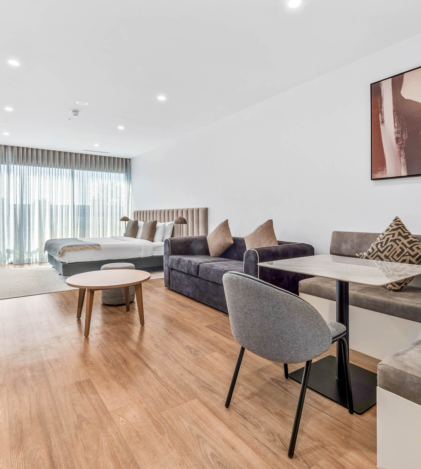 Living area with sofa, dining banquette and king bed by the balcony in a Deluxe Studio Apartment at Rambla @ Story House