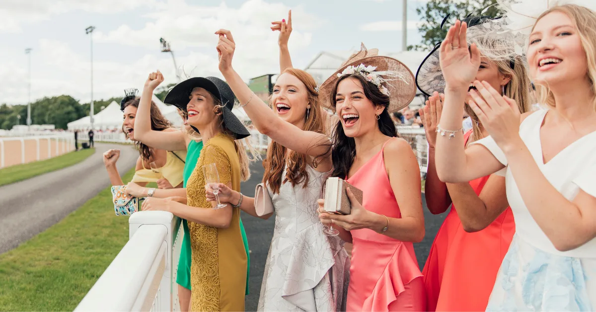 Racegoers in bright racewear and hats cheering at the rail on spring racing carnival race day