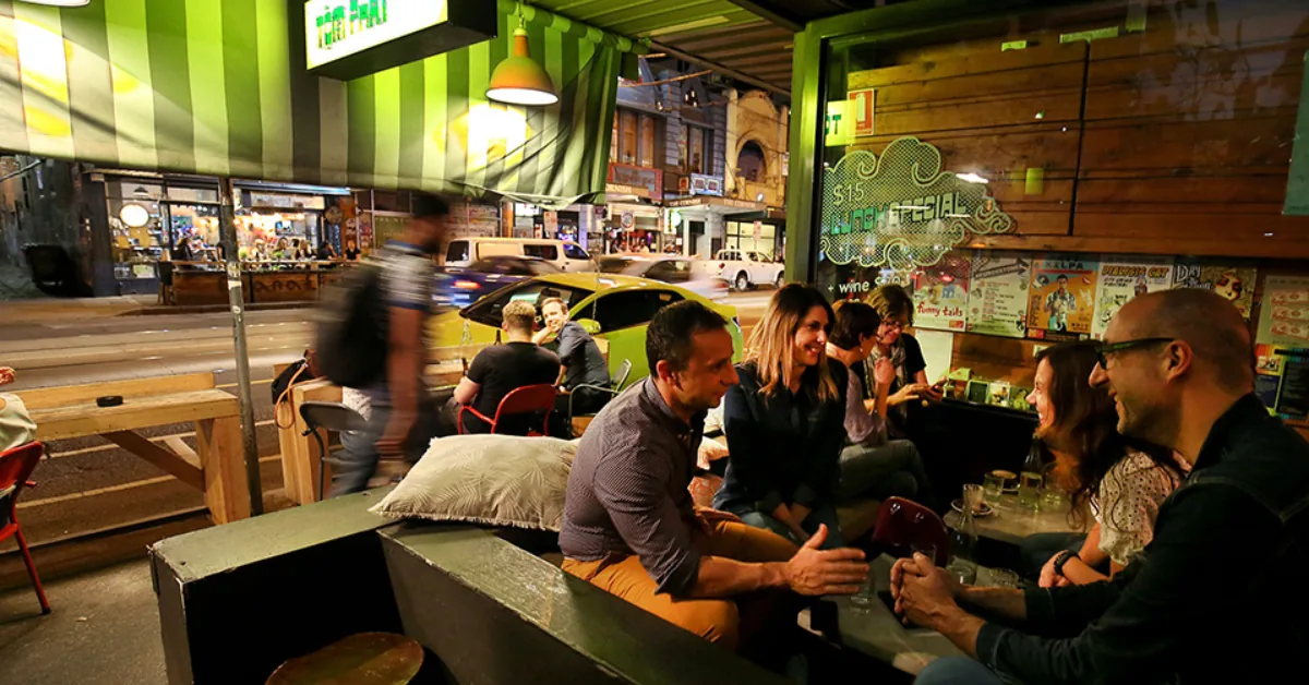 Friends drinking outside a bar on Sydney Road, Brunswick, on a warm evening