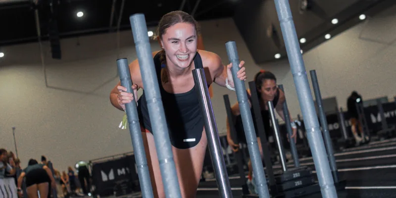 Smiling athlete pushing a weighted sled down the lane at a HYROX race