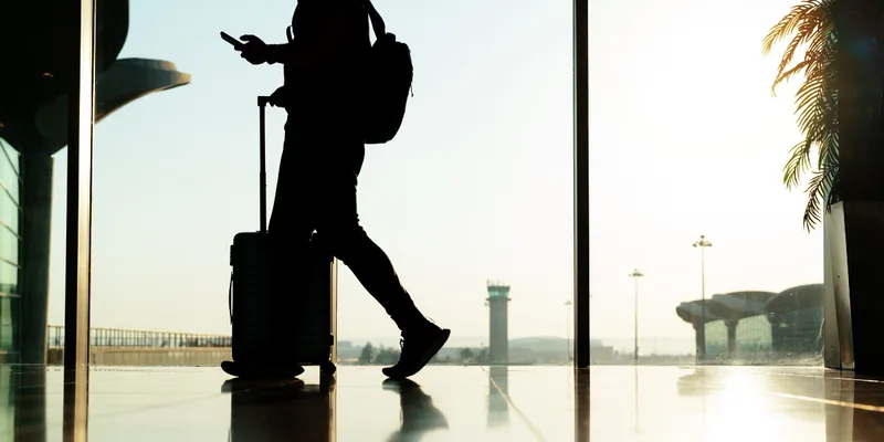 Traveller with a suitcase and phone crossing an airport terminal at dawn