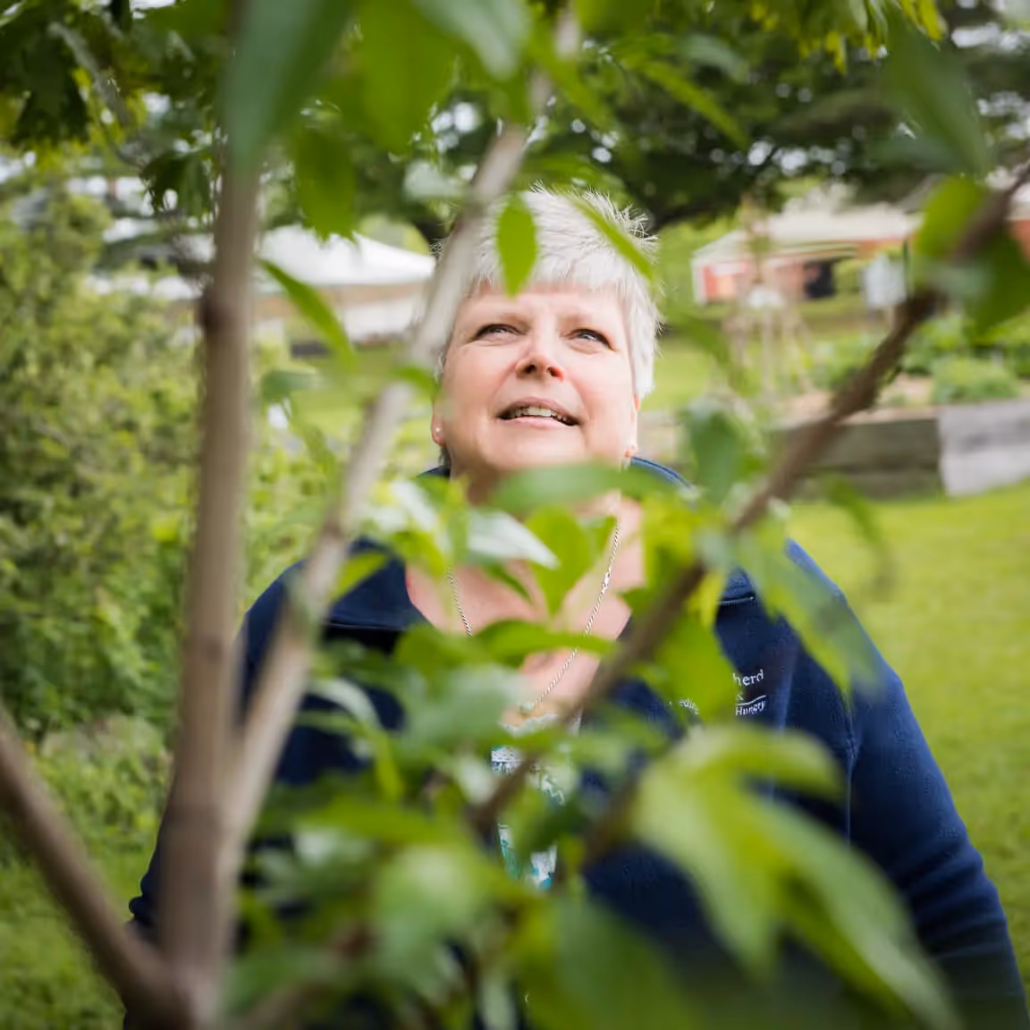 Smiling person viewed through green leaves in a garden setting