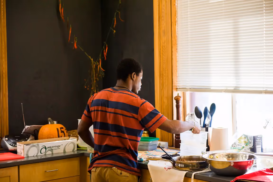 Person in striped shirt cooking in kitchen with pumpkin nearby