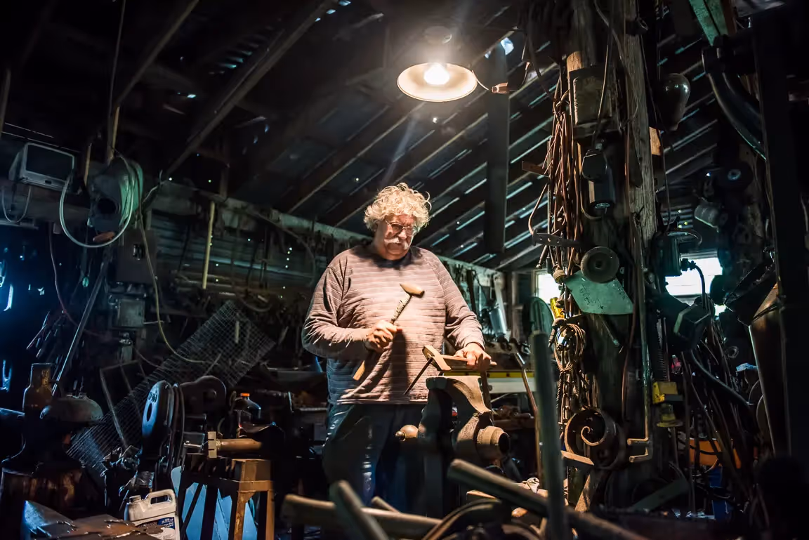 Elder craftsperson working in dimly lit, tool-filled workshop with vintage machinery