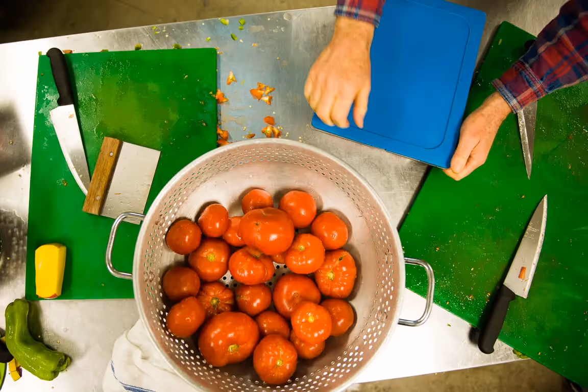 Fresh ripe tomatoes in colander with cutting boards and hands preparing food