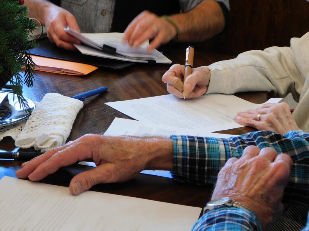 Hands writing on papers at a wooden table with a small Christmas tree