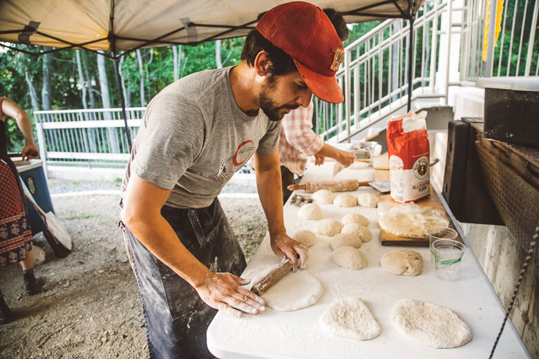 Baker in red cap kneading dough at outdoor food preparation station