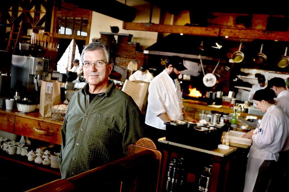 Chef standing in busy restaurant kitchen with staff cooking behind him