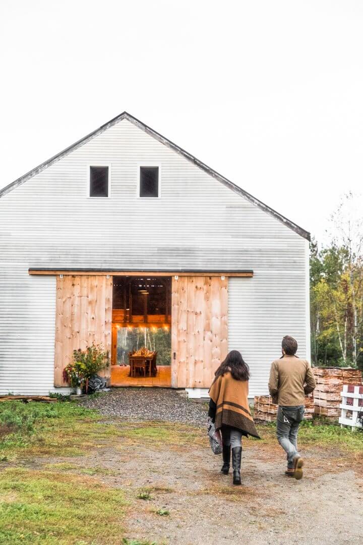 Two people walking towards a white barn with warm wooden sliding doors