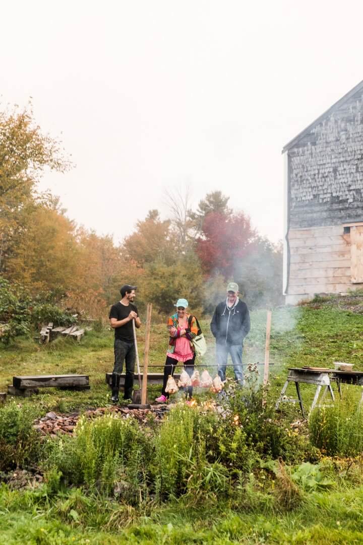 Three people working in garden with smoke rising near rustic barn