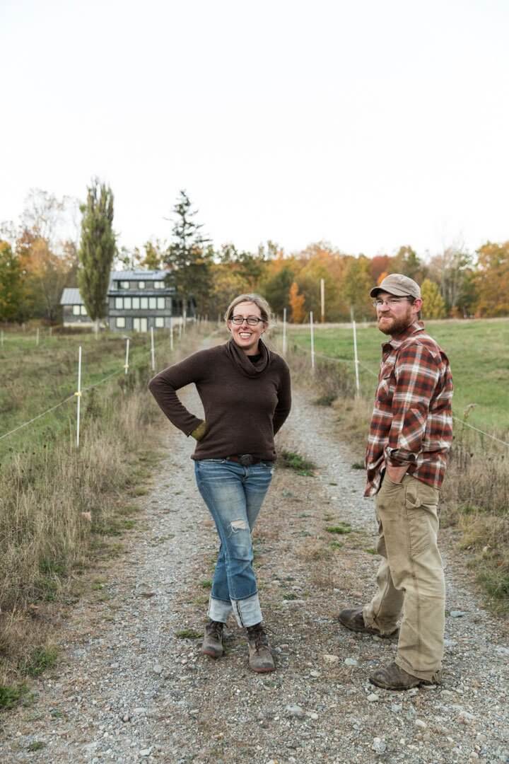 Two people standing on a gravel path with autumn trees and farmhouse background