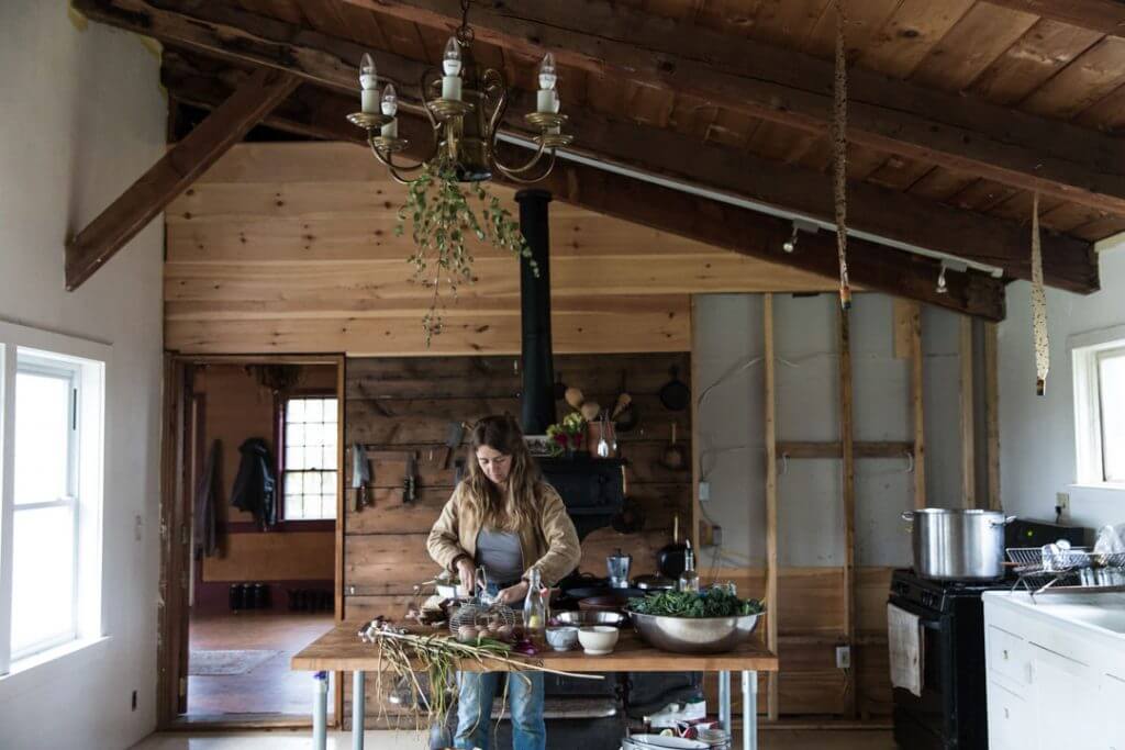 Woman preparing food in rustic wooden kitchen with hanging plants