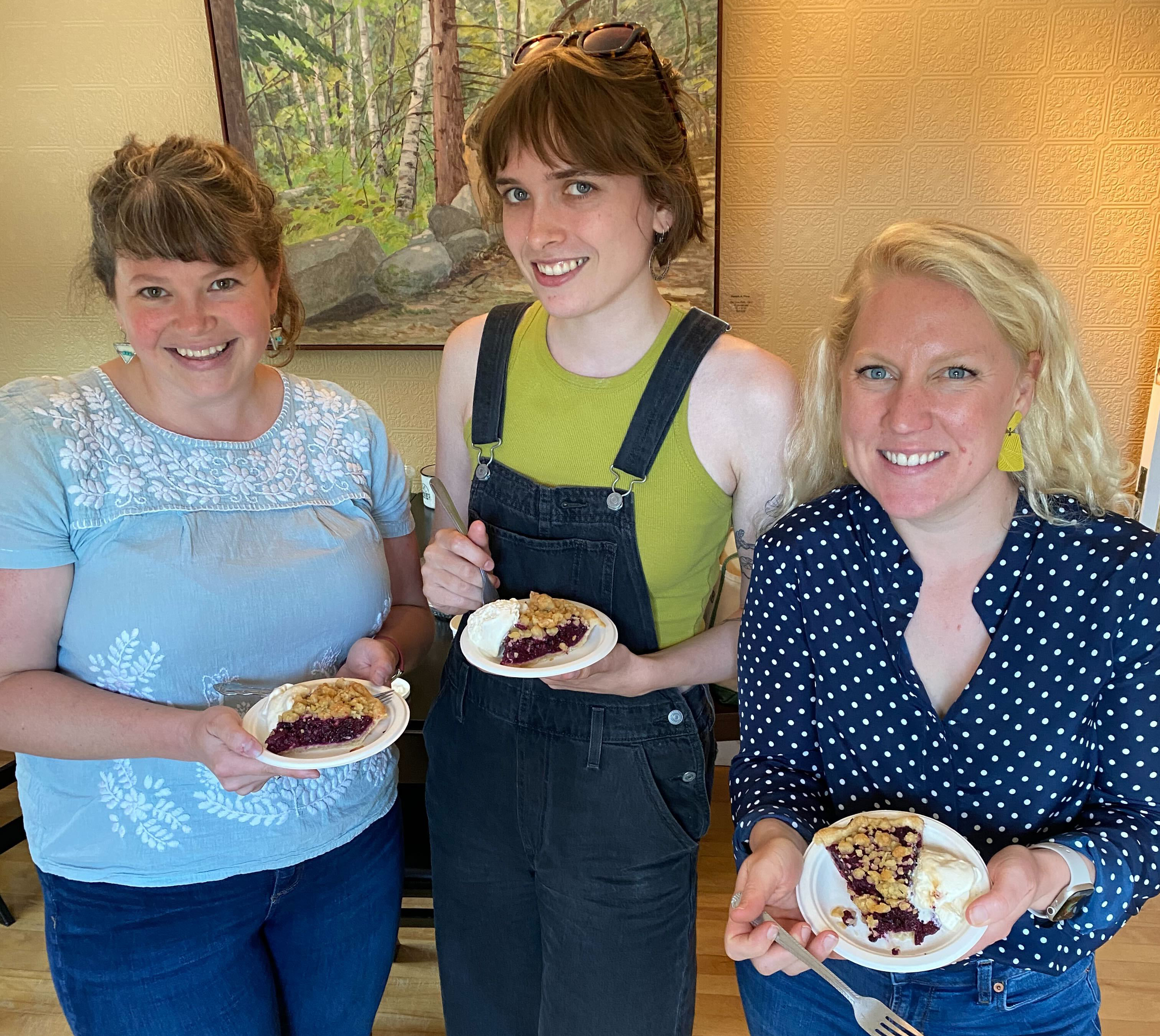 Three women smiling, holding plates with berry pie and ice cream