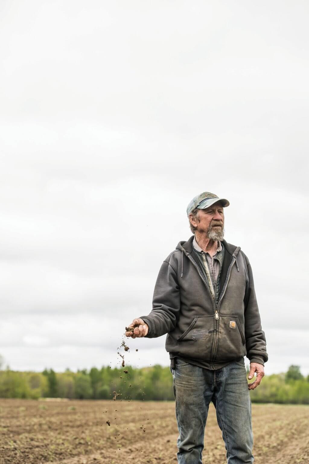 Farmer dropping soil from hand in plowed field on overcast day